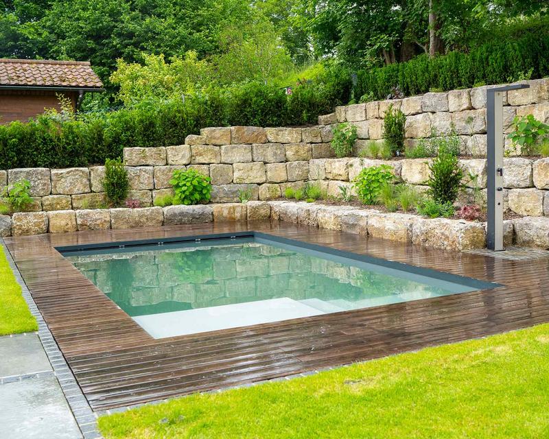 Aufnahme eines Hanggartens mit Pool und Holzterrasse. Umrundet von abgestuften Natursteinbauern im Hang
