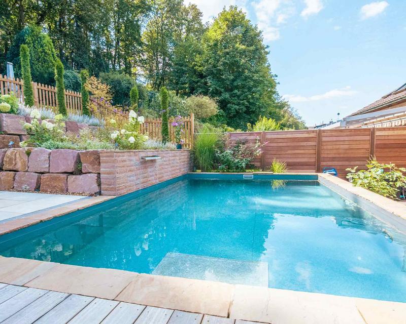 Biopool in Hanggarten, umrahmt von gepflasterter Terrasse und Holz Sichtschutz