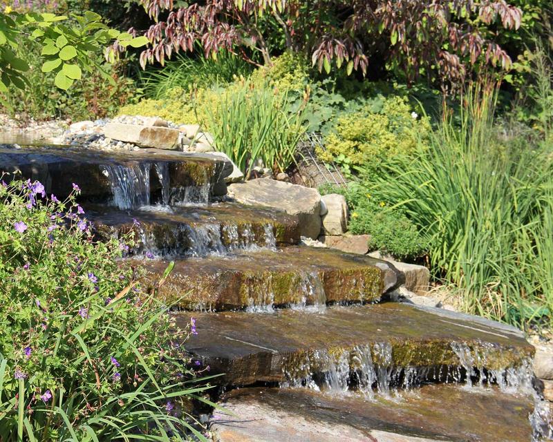 Bachlauf über große Natursteinstufen durch einen grünen Garten 