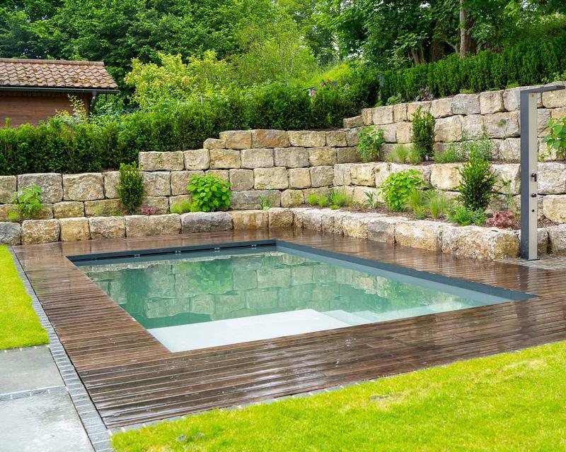 Biopool in einem Hanggarten umrandet von Holzterrasse und Steinstufen
