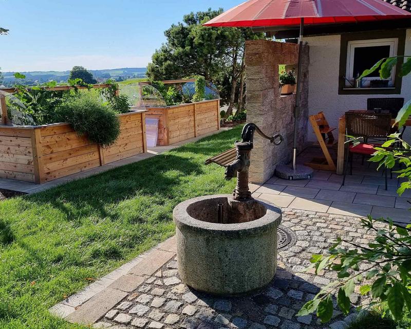 Pumpbrunnen mit Steintrog vor großen Hochbeeten