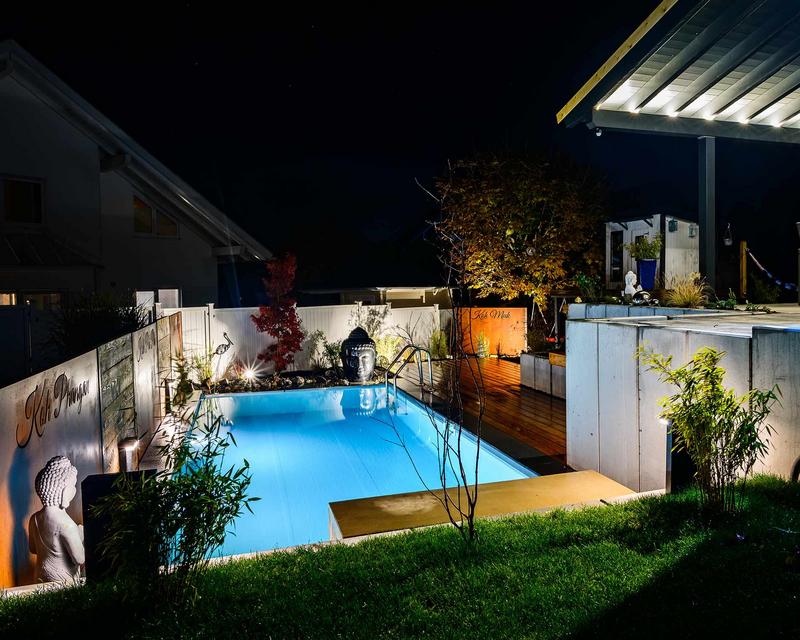 Nachtaufnahme eines Hanggartens mit beleuchtetem Pool und Gestaltungselementen