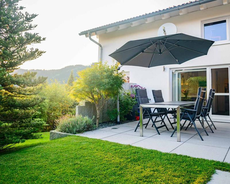 gepflasterte Terrasse mit Sitzgruppe und Sonnenschirm vor Einfamilienhaus