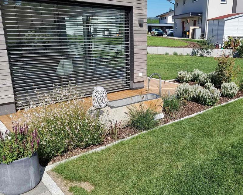 Aunfahme von Blumenbeeten rund um gepflasterte Terrasse an einem Wohnhaus