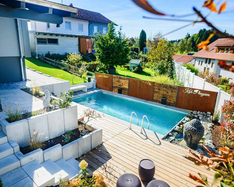 Luftaufnahme eines Hanggarten mit großem türkisenen Biopool und Metal Sichtschutz in Rostoptik