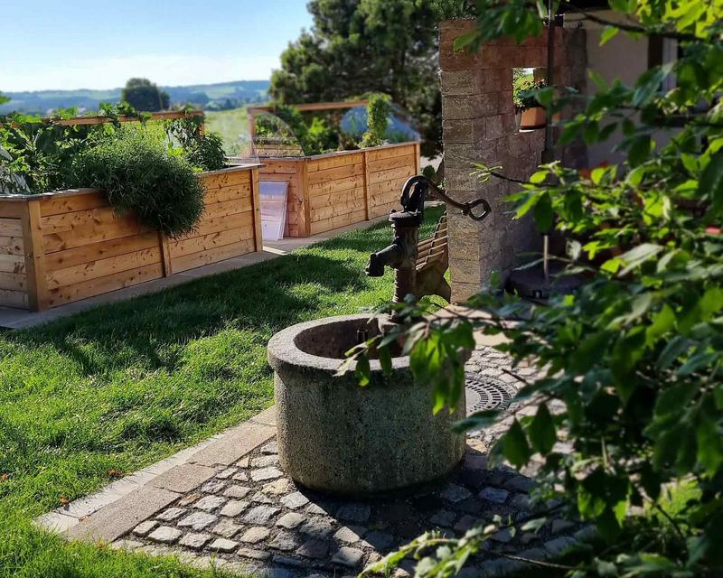 Pumpbrunnen mit Steintrog vor großen Hochbeeten