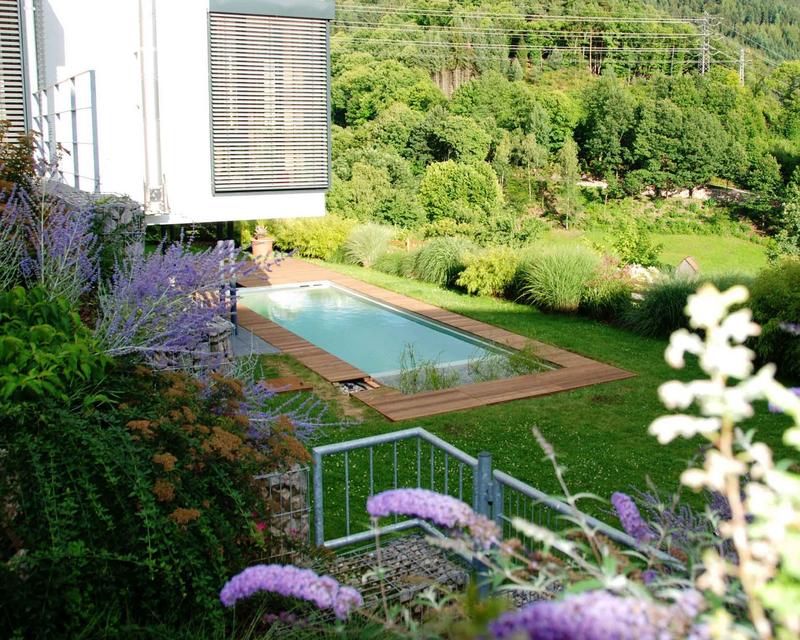 Hanggarten mit bunter Bepflanzung und Naturpool mit Holzterrasse