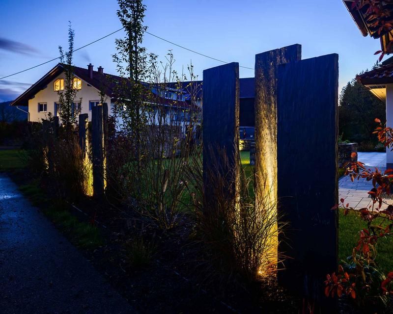 Abendliche Aufnahme eines Gartens mit beleuchteten Sichtschutzelementen