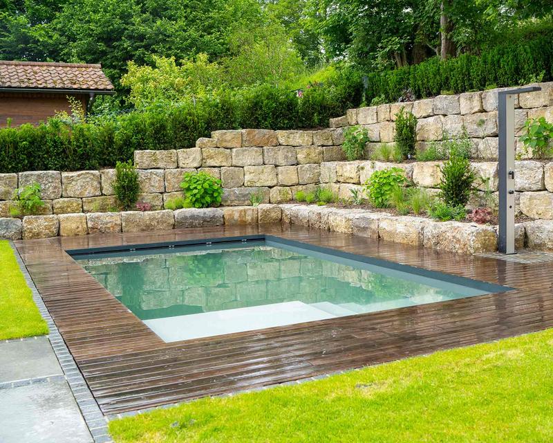 Aufnahme eines Biopools in einem Hanggarten, Umrandet von einer dunklen Holzterrasse