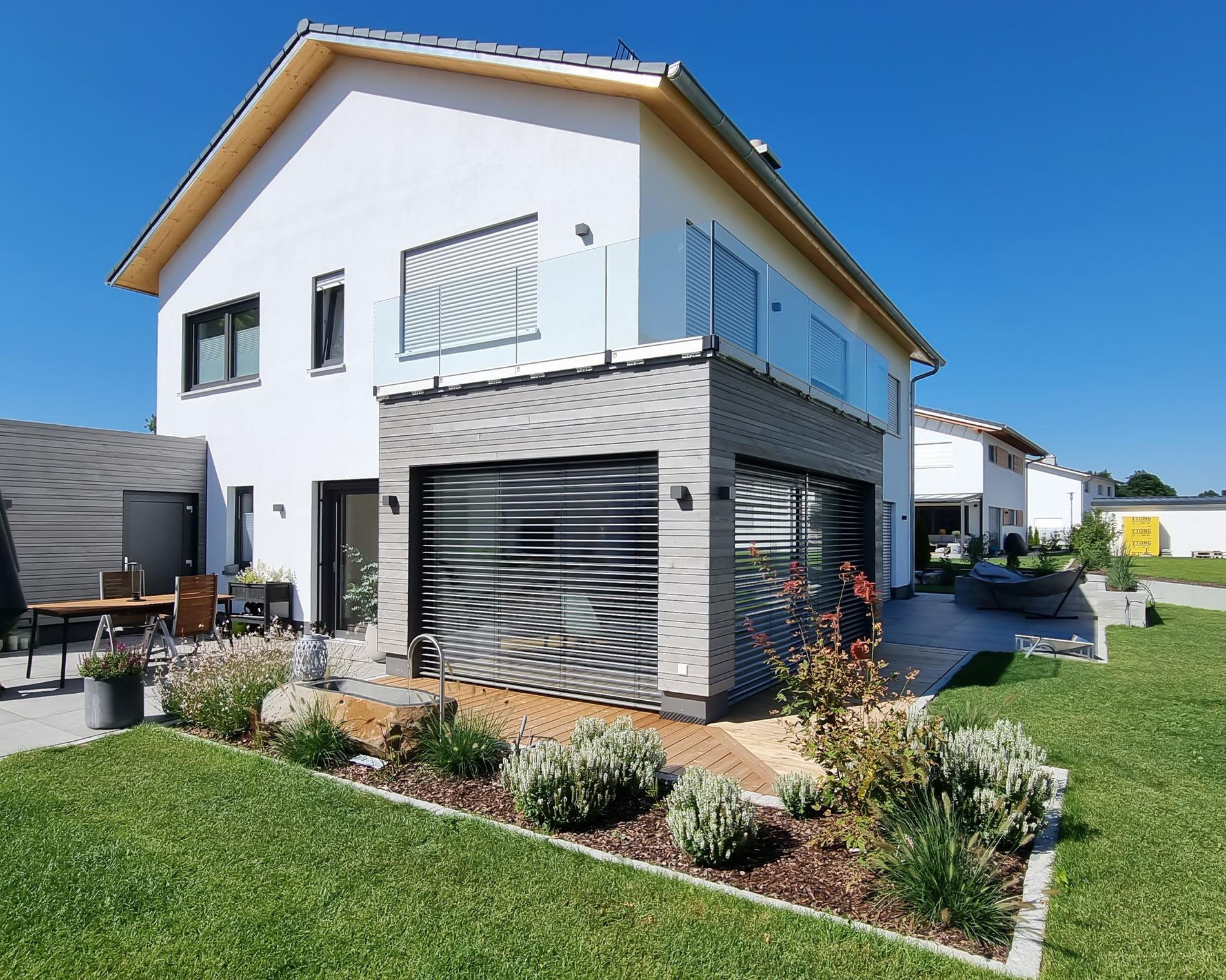 Aufnahme eines Wohnhauses mit Rasen und Blumenbeeten um die gepflasterte Terrasse herum